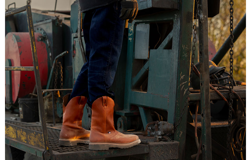 Un ángulo de primer plano de las botas de trabajo Lafayette para hombre en color marrón claro que usa un modelo en una plataforma de perforación.